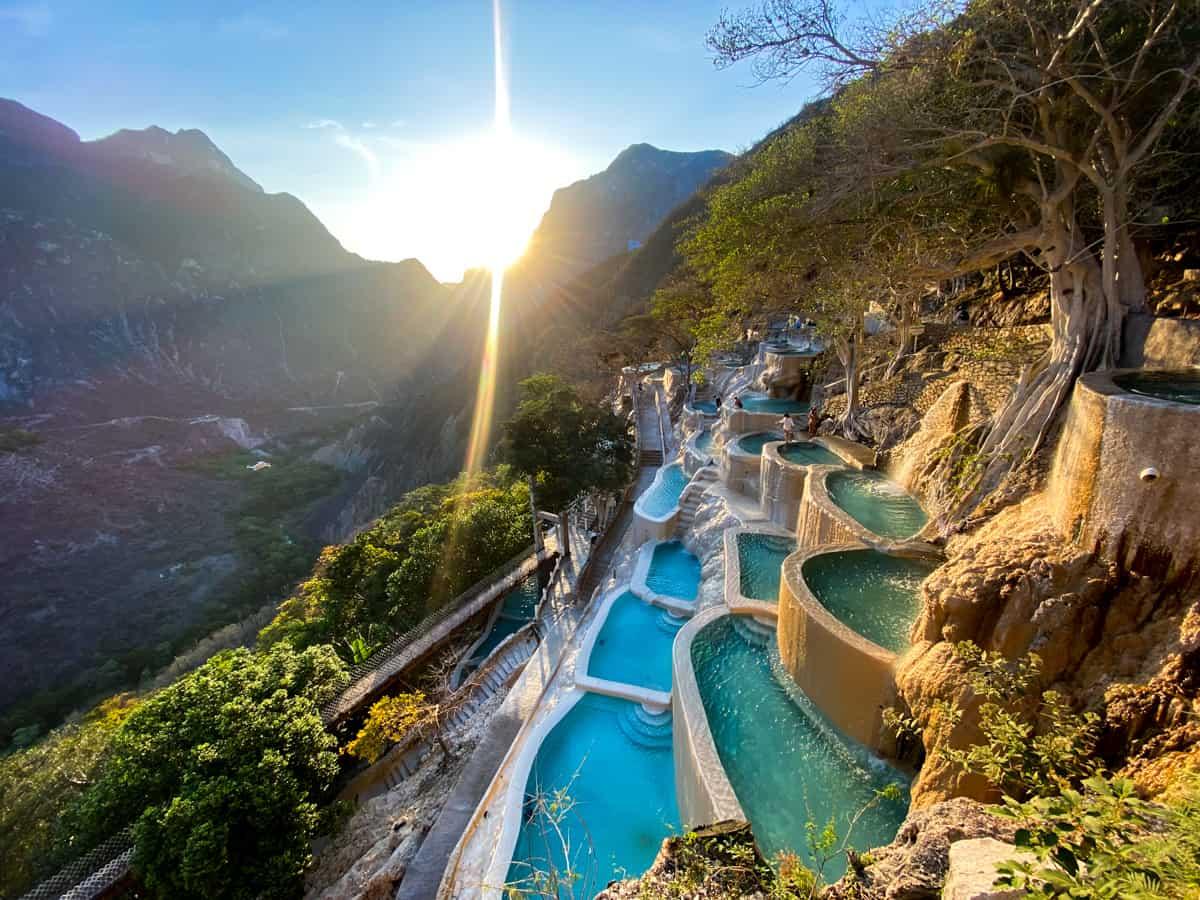 The thermal pools of Grutas Tolantongo stepped down the canyon wall at sunset, with the low sun breaking through the mountains
