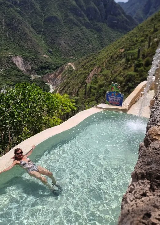 A swimmer floating in a cliff-edge pool at Grutas Tolantongo above the canyon