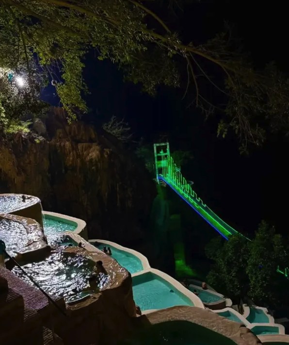 The thermal pools at Grutas Tolantongo after dark, with the suspension bridge lit green across the canyon