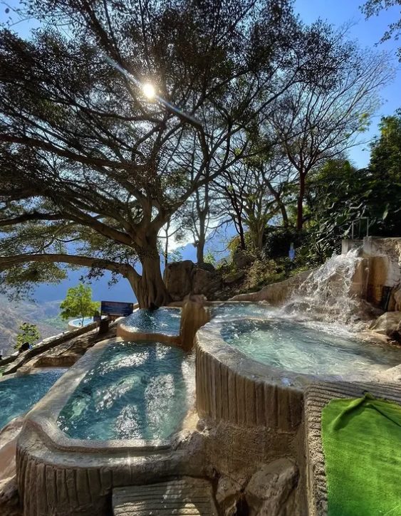 Two thermal pools at Grutas Tolantongo under a spreading tree, with water pouring in from the rock above